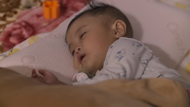 Asian baby sleeping peacefully with mouth open on futon on carpet