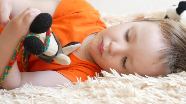One handsome little boy plays with a toy hare lying down on a soft plaid