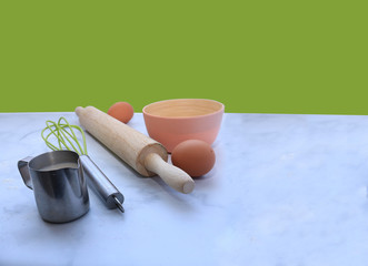 baking setup on marble surface  with a green background and copy space:  eggs, flour, milk & rolling pin