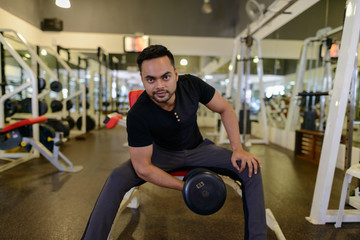 Plakat Full body shot of young bearded Indian man lifting weights at the gym