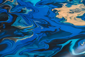 Fluorescent fluid art background in blue tints with gilding. Flowing ripple effect of liquid ink. Dark phantom blue with gold. Abstract texture of acrylic paints on canvas. Surreal blue color mixing.