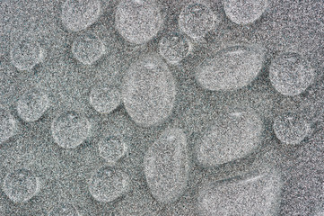 Abstraction with large drops of a transparent liquid on a silver mother-of-pearl surface, photographed close-up.