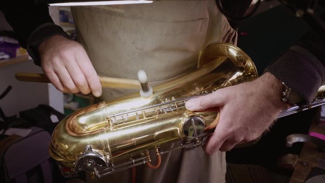 Skilled Instrument maker repairing dents in golden saxophone bell and bow with little hammer