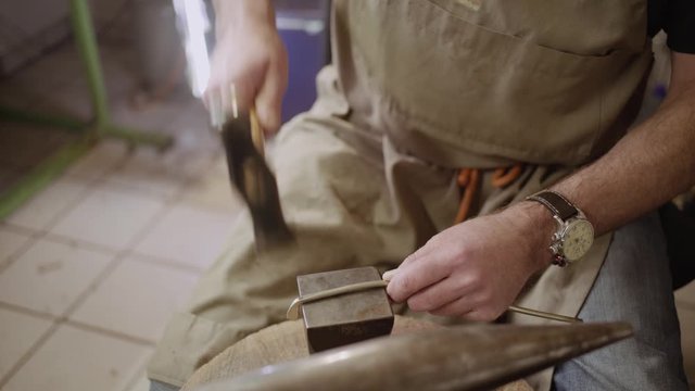 Instrument maker hammering metal bar into shape on anvil to forge a flute key for a transverse flute.