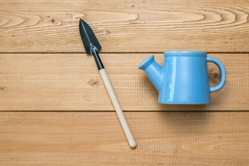 Watering can and blade for removing weeds on a wooden background.