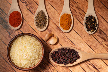 Ingredients for cooking pilaf: rice in a ceramic bowl, garlic, in wooden spoons on the table barberry, cumin, saffron and red pepper.