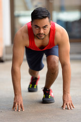 Full body shot of young bearded Indian man getting ready to run