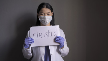 Beauty female doctor holds a paper sheet with inscription FINISHED. Joyful doctor reports the end...