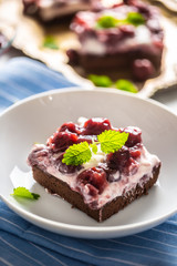 Portrait of a piece of brownie with a cream, cherries and fresh mint leaves on a plate