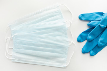 Three disposable masks for protection against viruses and blue disposable gloves on a white background top view. Minimum Outbreak and Pandemic Protection