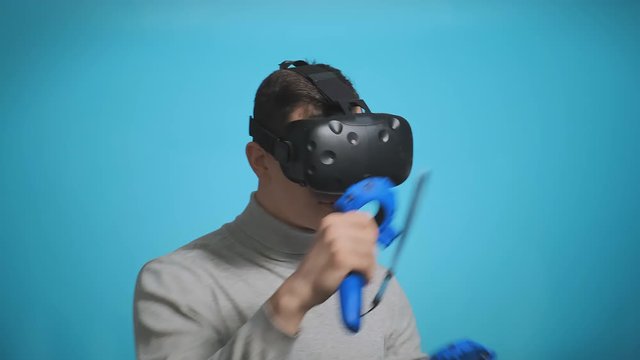 young guy plays virtual boxing match with modern reality headset and joysticks on light blue background slow motion