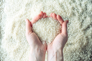 Women's hands hold a handful of white ground rice over a pile of cereals
