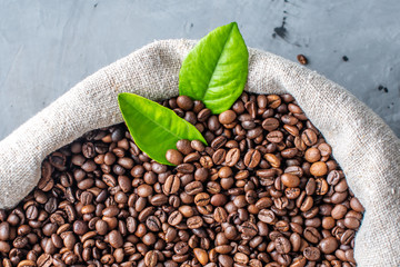 A burlap full of roasted aromatic coffee beans with green leaves. The view from the top