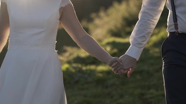 H&auml;nde des Brautpaars w&auml;hrend dem Gehen - Zusammenhalt in Zeitlupe bei Abendsonne