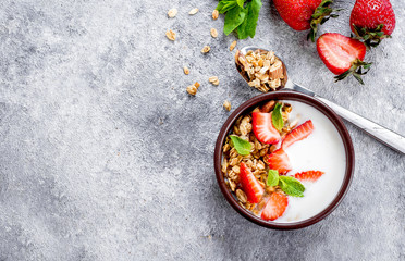 Food Background. Breakfast with yogurt, granola or muesli and strawberries on gray concrete table background. Healthy Diet Food Concept. Top view, copy space, flat lay