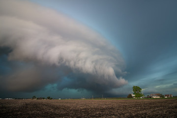 A large shelf cloud and severe thunderstorm approach fast over farms and fields.