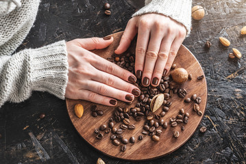 Beautiful neat female hands with nails covered with brown nail polish hold fragrant roasted coffee beans. Coffee manicure concept.