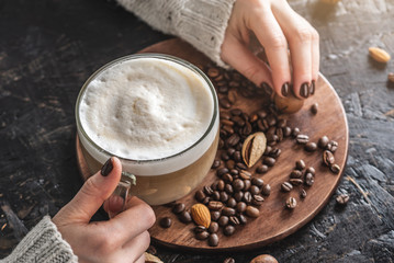 Women's hands in a warm sweater are holding a cup of fragrant latte. The nails are coated with brown nail polish. Coffee manicure. Breakfast or a break in a cozy cafe. Top view