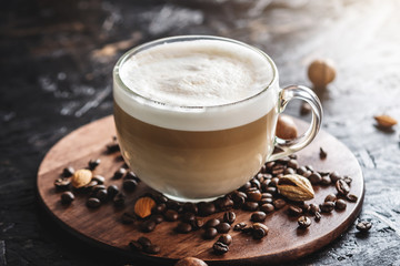 Aromatic delicious latte in a transparent Cup on a brown wooden tray. There are coffee beans and nuts nearby. Breakfast or a coffee break in a cozy cafe