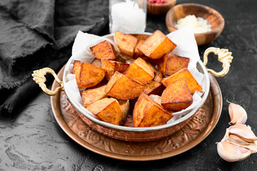 Roasted potato wedges with garlic and salt in copper pan.