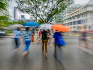 A motion blurred shot of pedestrians crossing a street on a rainy day in downtown Singapore, giving...