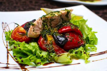 Warm salmon salad on a pillow of fresh grilled vegetables with green juicy lettuce leaves. Restaurant serving.