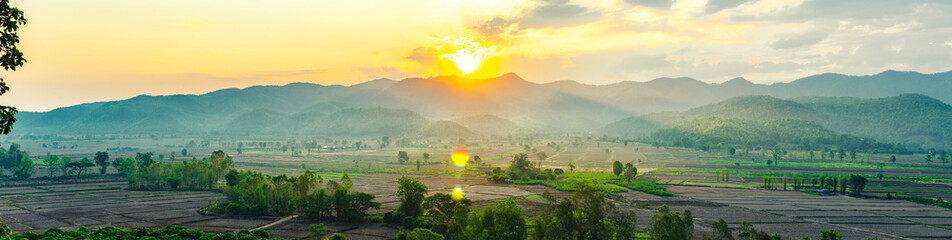 The beautiful panorama landscape of the sunrise, The sun's rays through at the top of the hill  over the tree in the rice fields, Chiang Rai Northern  Thailand.