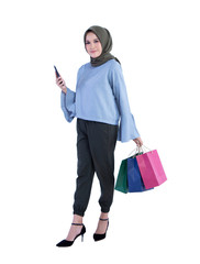 Young muslim woman holding phone cell looking at camera and carrying a shopping bag isolated on white background
