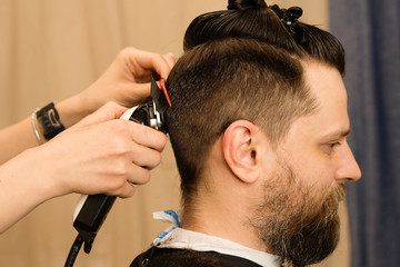 Male haircut electric razor. Hand of hairdresser shaves hair with electric shaver. Hipster man getting a trendy haircut with a hair clipper and comb. Barber services. Hairstyling process.