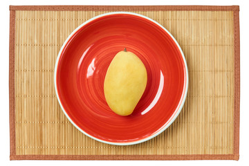 pale yallow mango on a red plate on a cane tablecloth