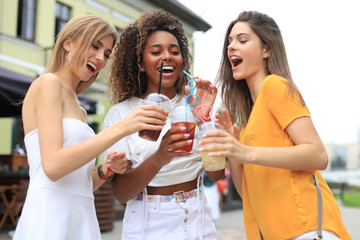 Three trendy cool hipster girls, friends drink cocktail in urban city background.