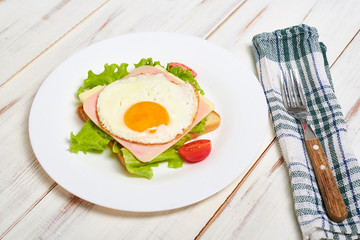 Toast with ham, egg and tomato on a plate on a light wooden background.