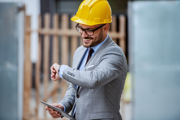 Attractive elegant caucasian smiling architect in suit, with eyeglasses and helmet on head standing...
