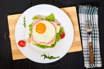 Toast with ham, egg and tomato on a plate on a black background.