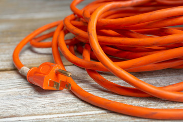 A closeup view of a wrapped orange extension cord, showing the male prong connector on the left side of the frame, on a wooden surface.