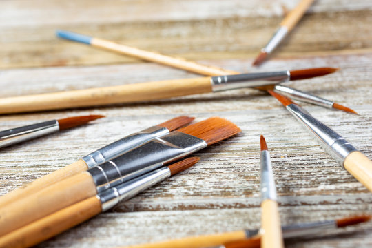 A closeup view of a pile of different sized paint brushes, on a wooden surface.