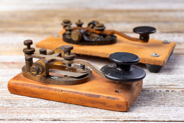 A closeup view of two vintage ham radio morse code straight key units, on a wooden surface.