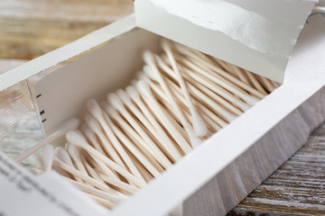 A closeup view of a box full of cotton swabs on a wooden surface.