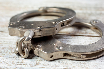 A closeup view of a pair of metal handcuffs, on a wooden surface.