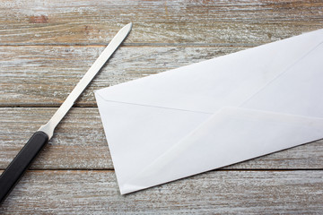 A top down view of a business envelope and letter opener tool, on a wooden table surface.