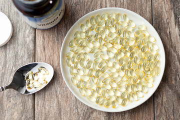 A top down view of a plate filled with Vitamin D or D3 gel pills. Some pills are on a spoon and there is a bottle adjacent.