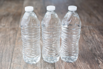 A view of three plastic water bottles with no label, on a wooden table surface.