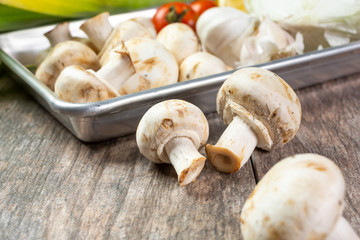 A view of several fresh white button mushrooms on a metal tray, in a still life setting.