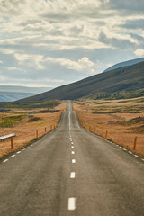 Travelling Iceland in Autumn. Amazing view of empty road passing through beautiful landscape in Iceland, dramatic cloudy sky