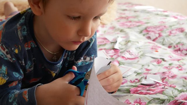 A little boy carefully cuts paper geometric figures