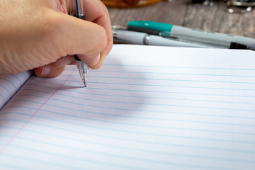 A view of a hand using a ball point pen to write on a lined paper.