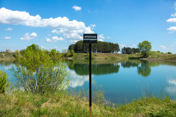 No swimming sign (in Russian) on the shore of the protected freshwater lake, in the background - a...
