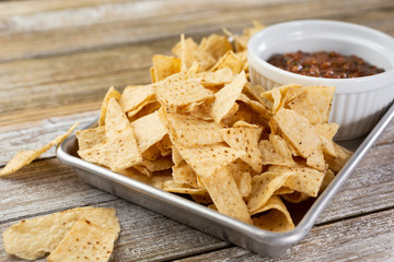 A view of a metal tray with corn tortilla chips and a bowl of salsa.
