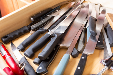 A view of a drawer full of kitchen knives and other sharp cutlery utensils.