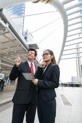 Mature businessman and young Asian businesswoman using digital tablet together in the city